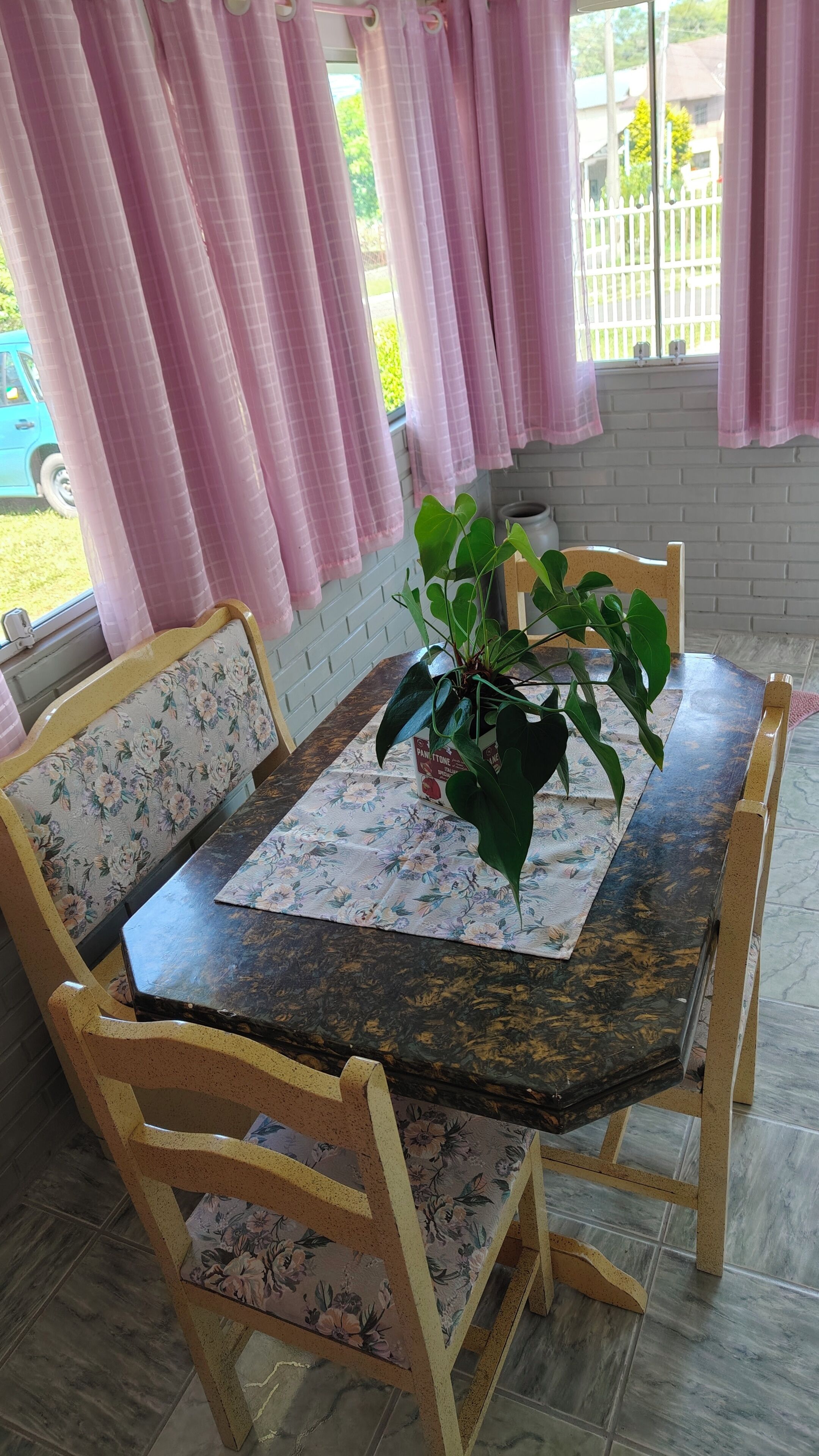 A dining area with a floral-patterned bench, a table with a placemat, and a potted plant.