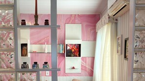 Un dormitorio con una decoración en tonos rosa y blanco, una cama con cubrecama rosa, un aparador y una estantería con objetos decorativos.