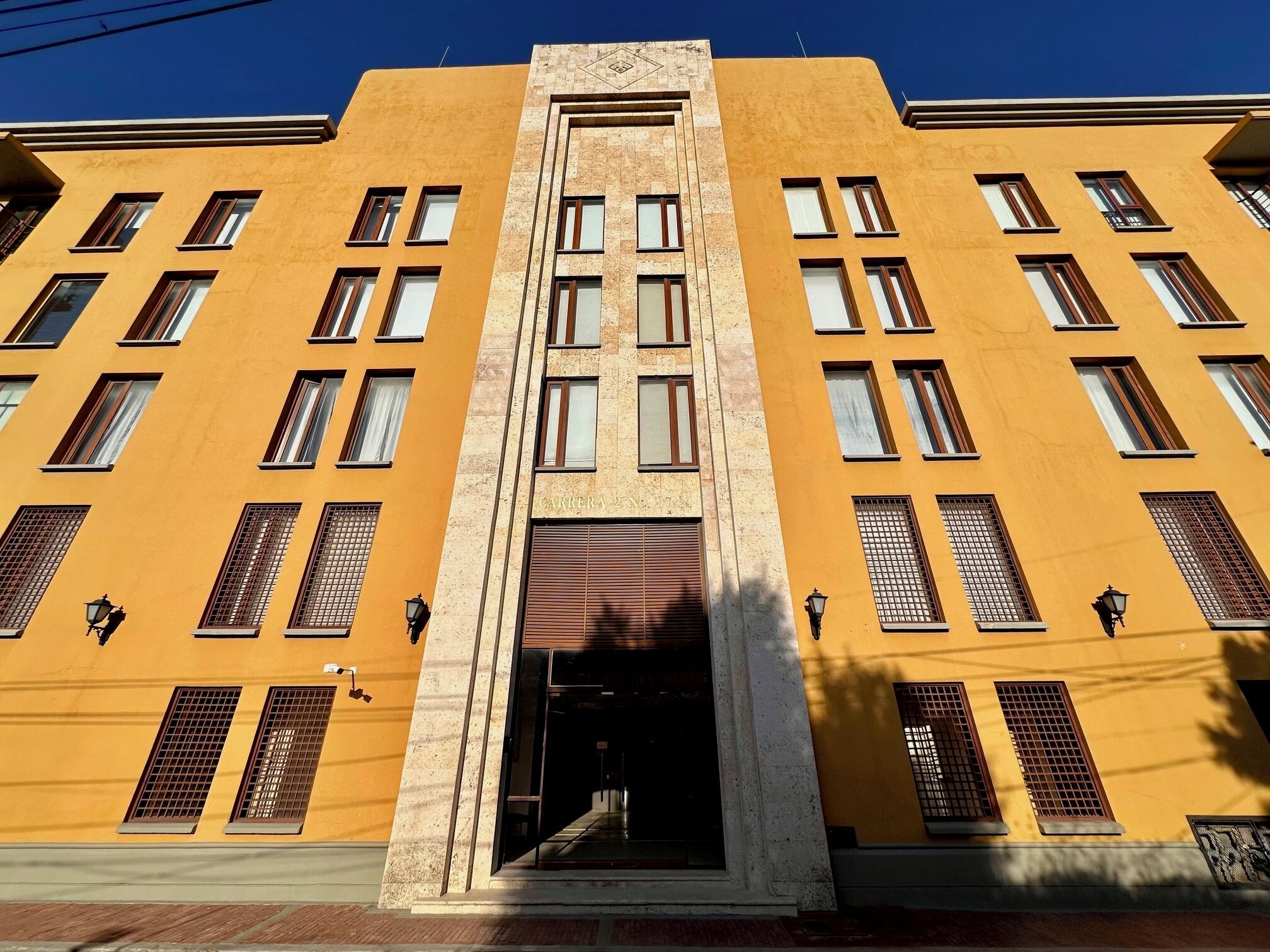 Un edificio con entrada central, varias ventanas y fachada amarilla.