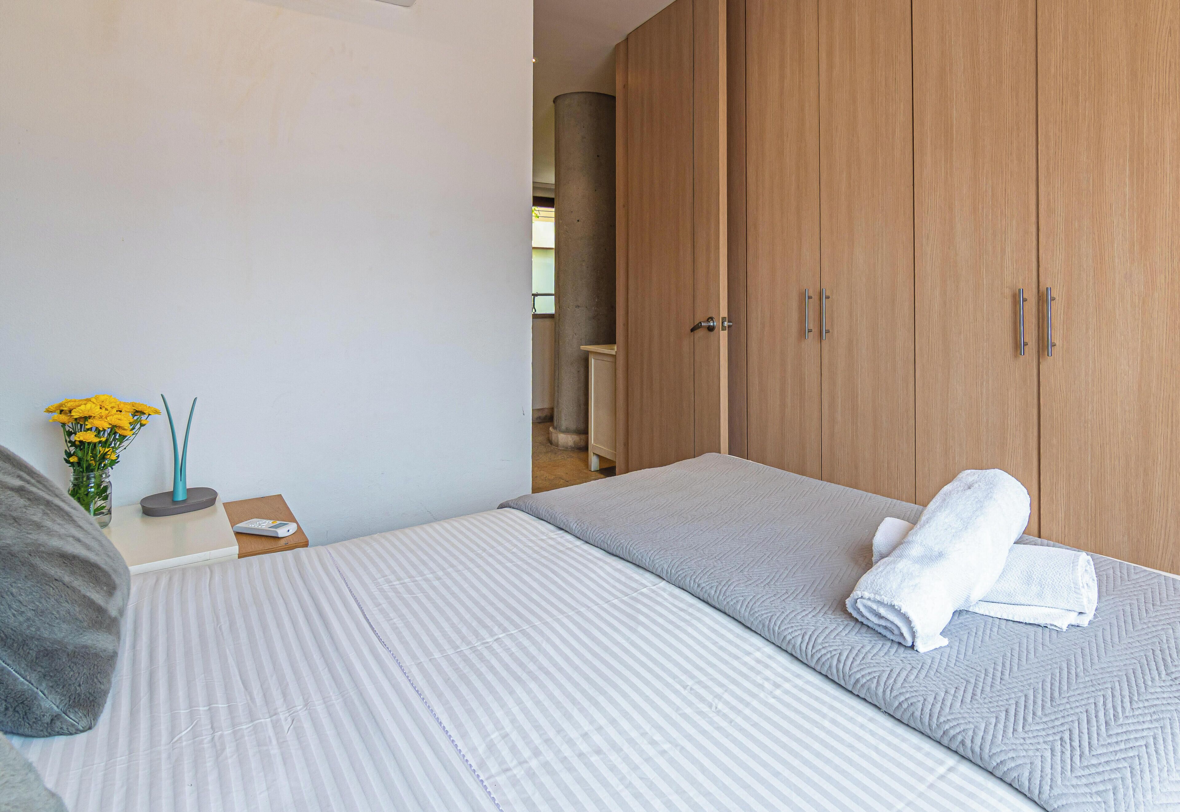 Une chambre avec deux lits, une armoire en bois, une table de chevet ornée d’un vase de fleurs et une petite table de nuit.