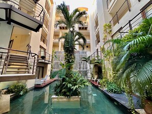 A multi-level building with a central courtyard featuring a pool, surrounded by lush greenery and a waterfall. - Luxury Boutique Apartments by Xarm Apartments (Santa Marta)