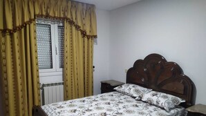 A bedroom with a wooden bed, a nightstand, a chair, and a window with curtains. - Walnut House with Private Pool (Gondufe)