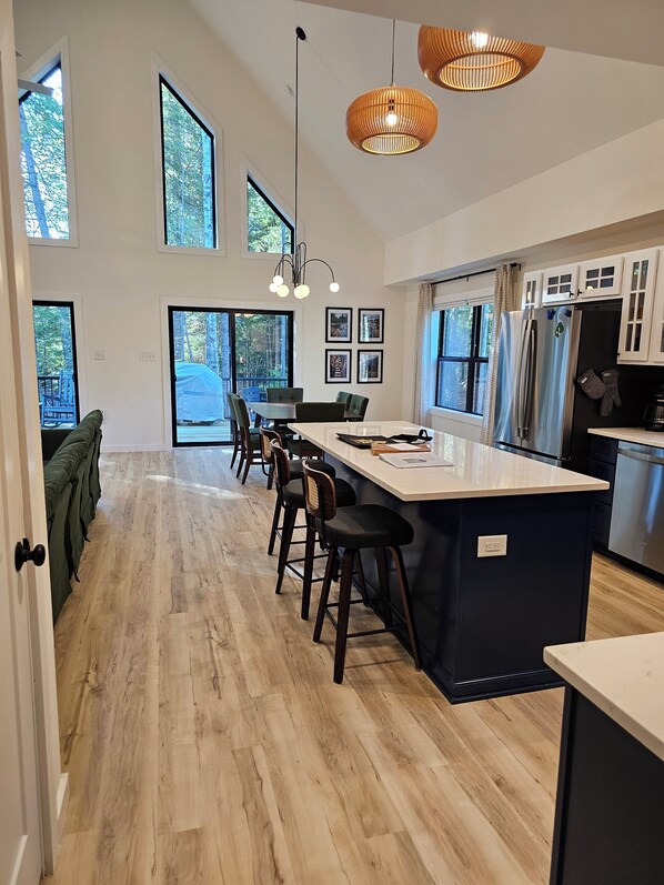 Una cocina moderna con una isla central, taburetes de bar y ventanas amplias.