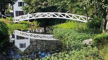 A white bridge over a pond with lush greenery and a building in the background.