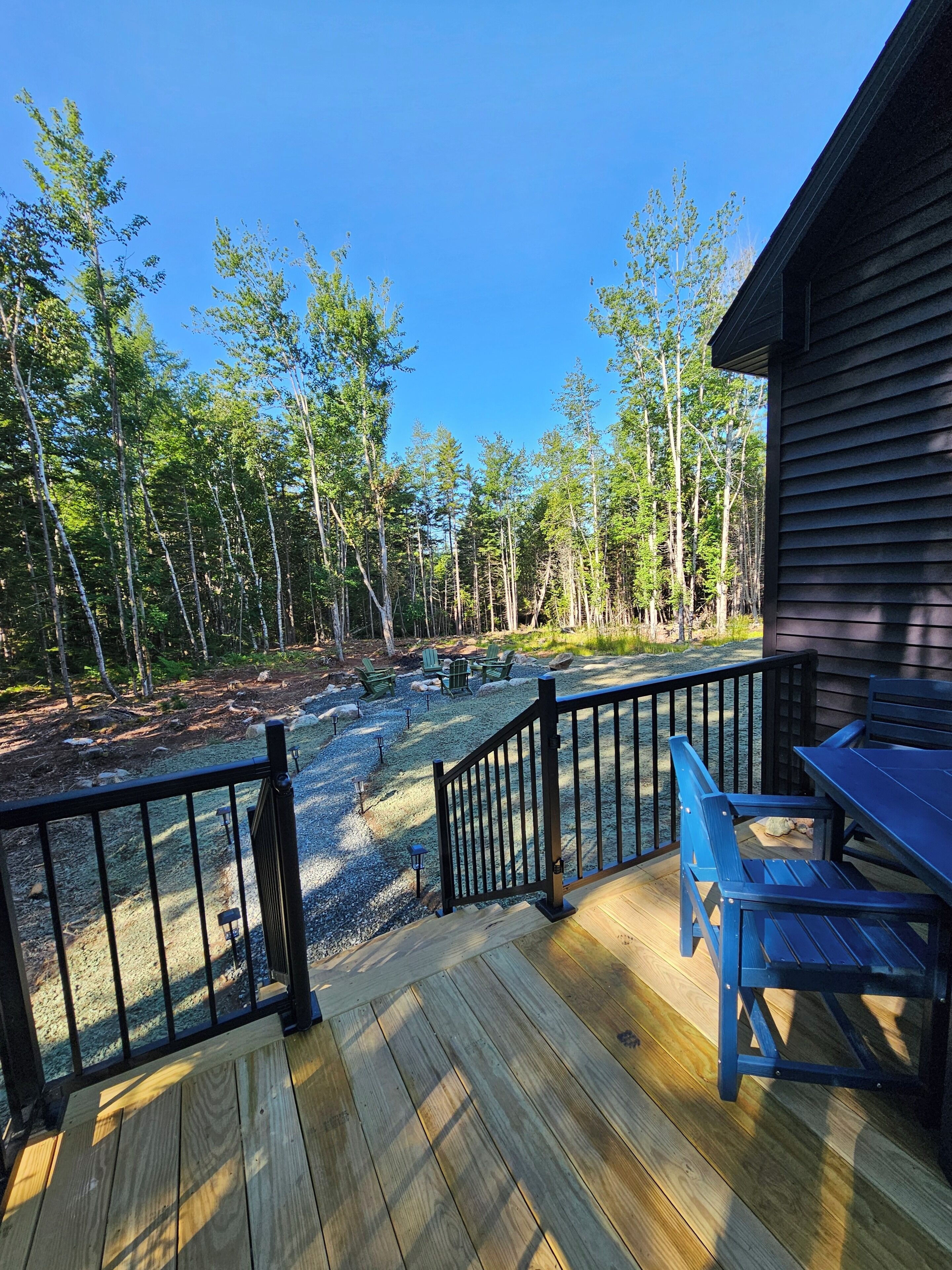 A wooden deck with a railing, outdoor seating, and a view of a forest.
