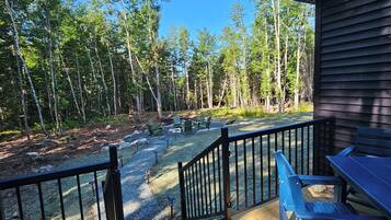 A wooden deck with a railing, outdoor seating, and a view of a forest.