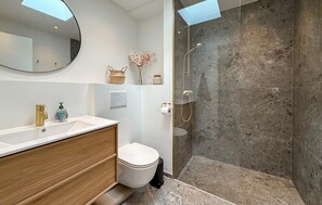 Um banheiro moderno com toucador branco, vaso sanitário, chuveiro com porta de vidro e um espelho grande.