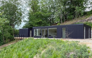 Eine moderne, dunkel gefärbte Holzhütte mit großen Fenstern, umgeben von dichtem Wald.
