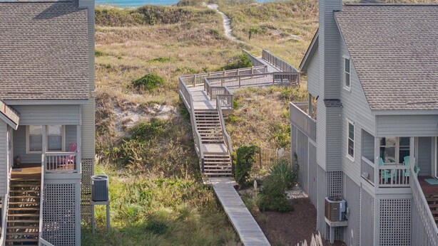 Ein Küstenanwesen mit einer Holzterrasse, die zu einem Strand führt, umgeben von grasbewachsenen Dünen.
