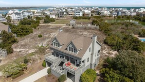 Ein zweigeschossiges Haus mit Balkon, umgeben von einem angelegten Garten und Blick auf eine Küstenlandschaft mit weiteren Häusern.