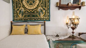 Ein Bett mit zwei gelben Kissen, einer Wandteppich, einer an der Wand befestigten Uhr und einem Tisch mit einer Lampe.