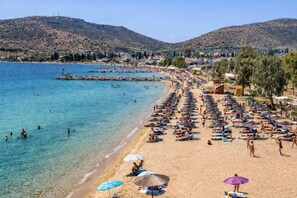 Une plage avec une eau d’un bleu limpide, des chaises longues, des parasols et une chaîne de montagnes en arrière-plan.