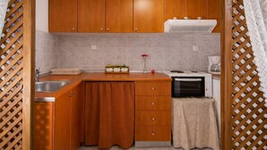 A kitchen with wooden cabinets, a sink, a microwave, and a small table with a cloth. - Byzantine Vibe - Seaside Cozy Stay Near Volos (Volos)