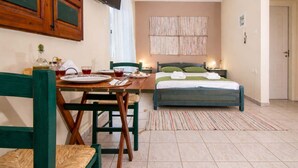 A room with a bed, a table with chairs, a television mounted on the wall, and a window with curtains. - Village Vibe - Seaside Stay w Balcony Near Volos (Volos)