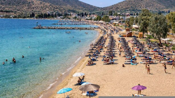 A beach with clear water, umbrellas, and people. - Village Vibe - Seaside Stay w Balcony Near Volos (Volos)