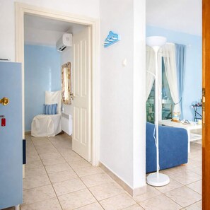 A hotel room with a bed, a bedside table, a lamp, a window with curtains, and a door leading to another room. - Beach Vibe - Seaside Stay w Balcony Near Volos (Volos)
