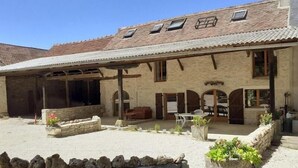 Ein Steinhaus mit überdachter Terrasse, Außenbestuhlung und einer Steinsäule.