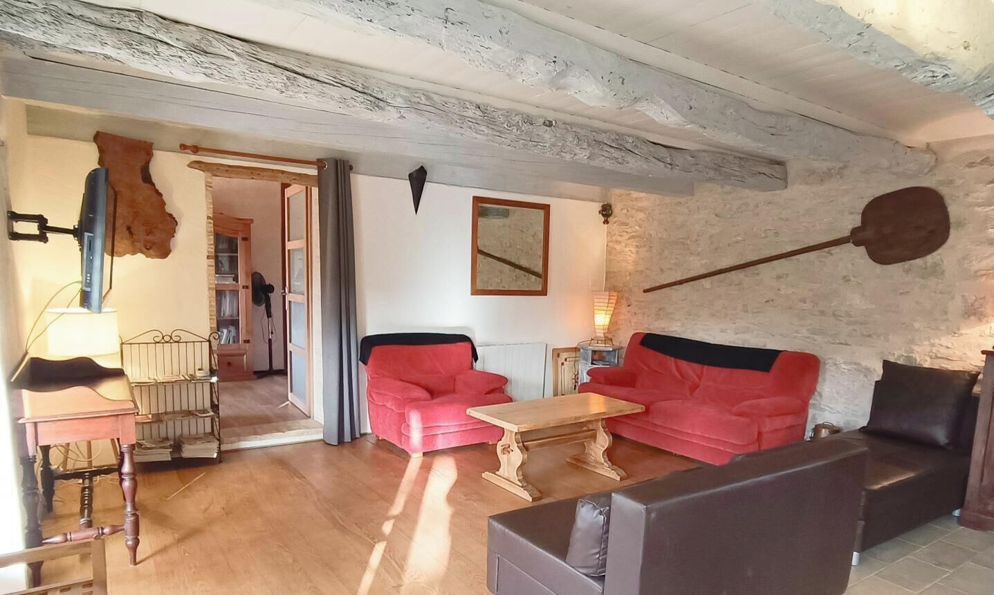 Ein Wohnzimmer mit Holzboden, einem roten Sofa, einem braunen Sofa, einem Holztisch und einem Fernseher.