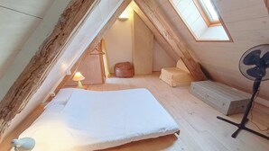 Ein Schlafzimmer im Loftsstil mit Bett, Standventilator und Dachfenster.
