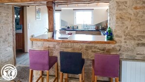 Eine rustikale Küche mit Steinwand, Holzbalken und einer Bar mit violetten Stühlen.