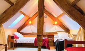 A room with two beds, wooden beams, and a sloped ceiling with skylights. - Gîtes de France® - La Grange de Malou (REILHAGUET)