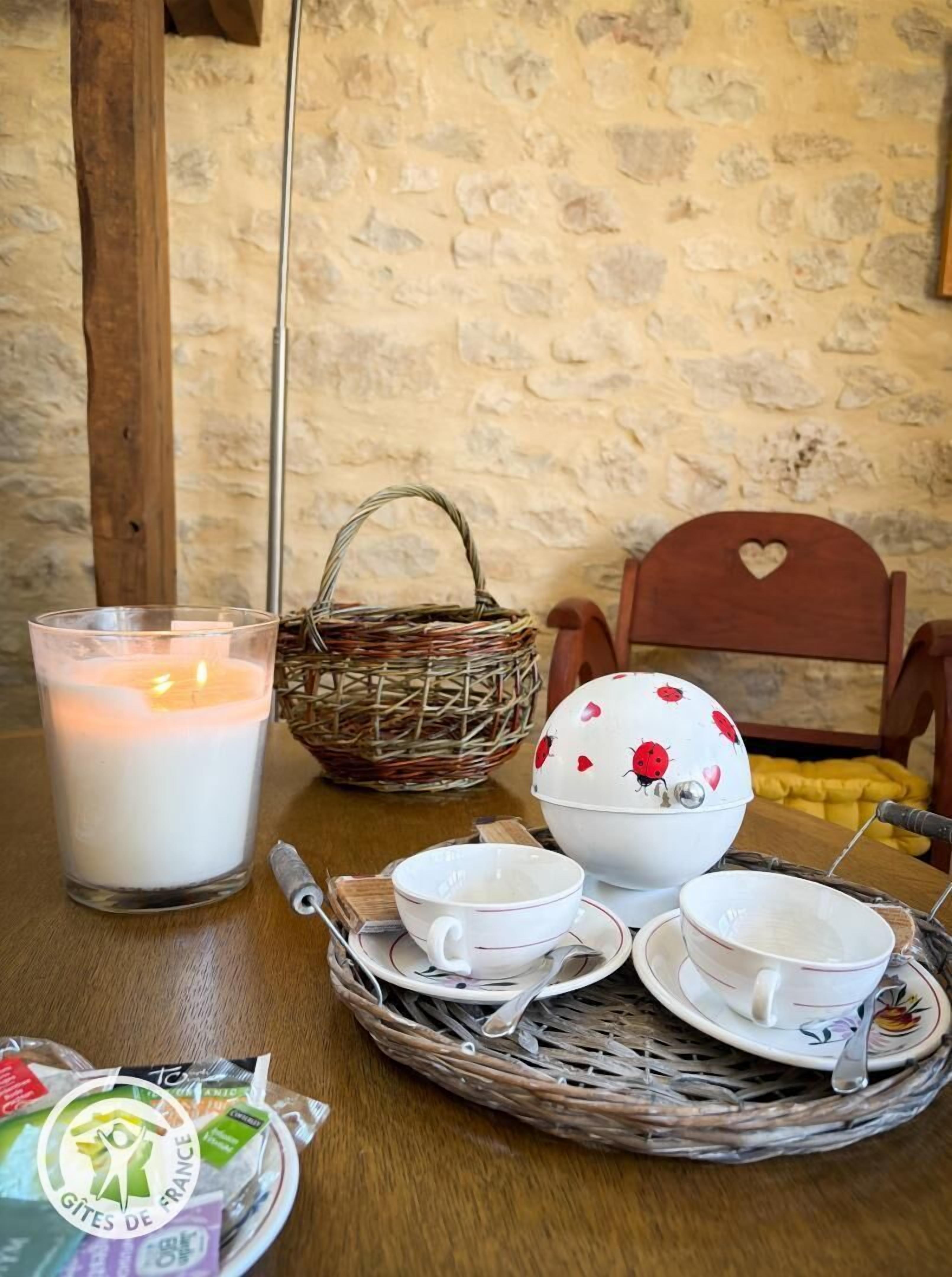 Een tafel met een brandende kaars, een rieten mand, een theeservies en een decoratieve stoel.