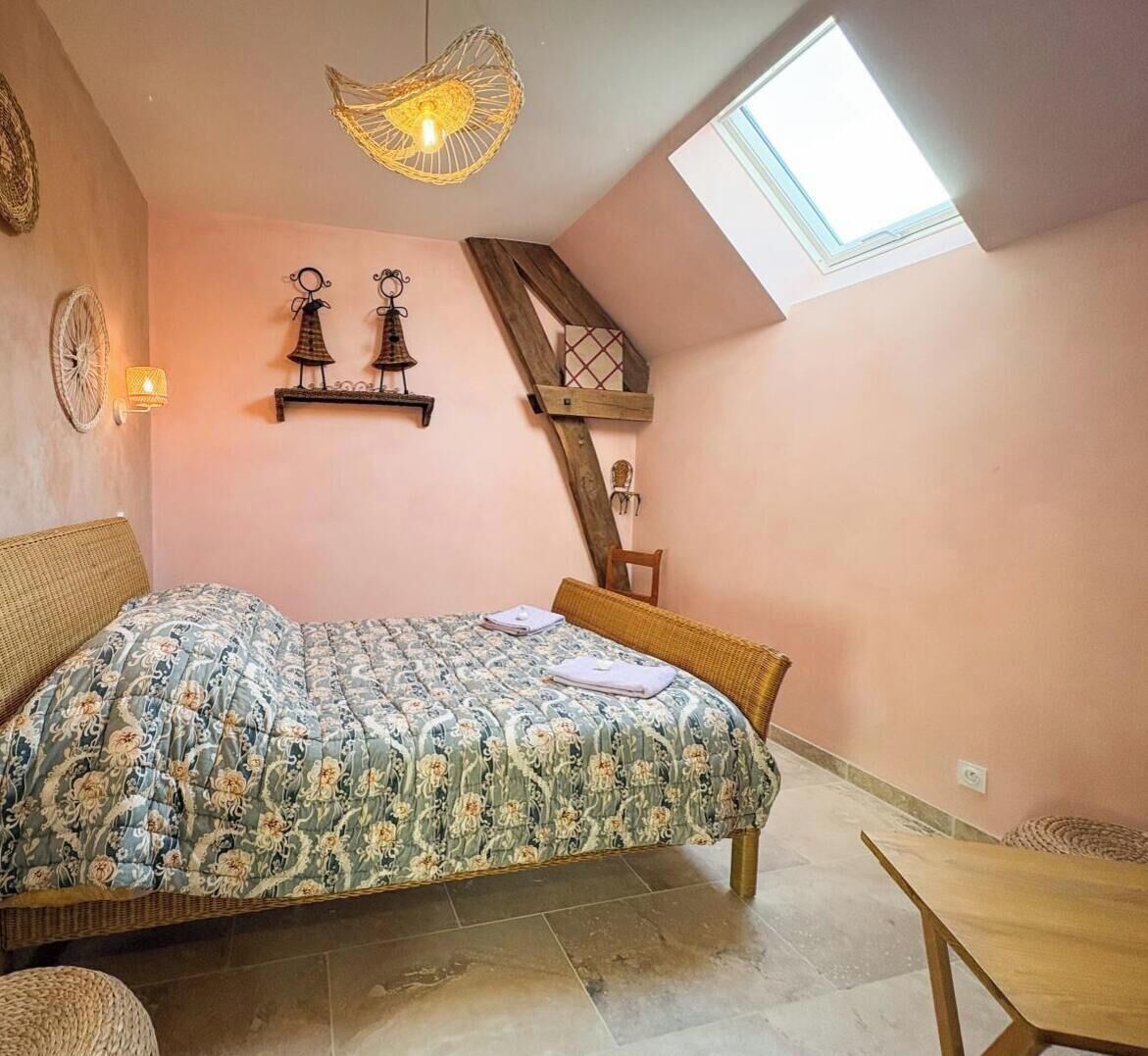 A bedroom with a sloped ceiling, a bed with a floral bedspread, a wooden chair, a small table, and a skylight.