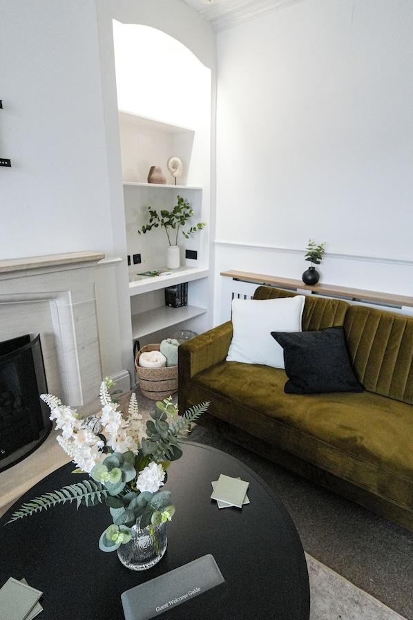 A modern living room with a sofa, a fireplace, a coffee table with a vase, and a bookshelf.