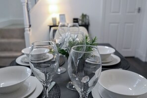 A dining table set with clear glassware and white plates, with a staircase and a door in the background. - Cosy 3-Bed Home | Parking | Ideal for Work Stays (Brierfield)