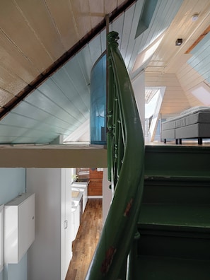 Een meerlaags interieur met een trap, een bed en uitzicht op een houten vloer en een raam.