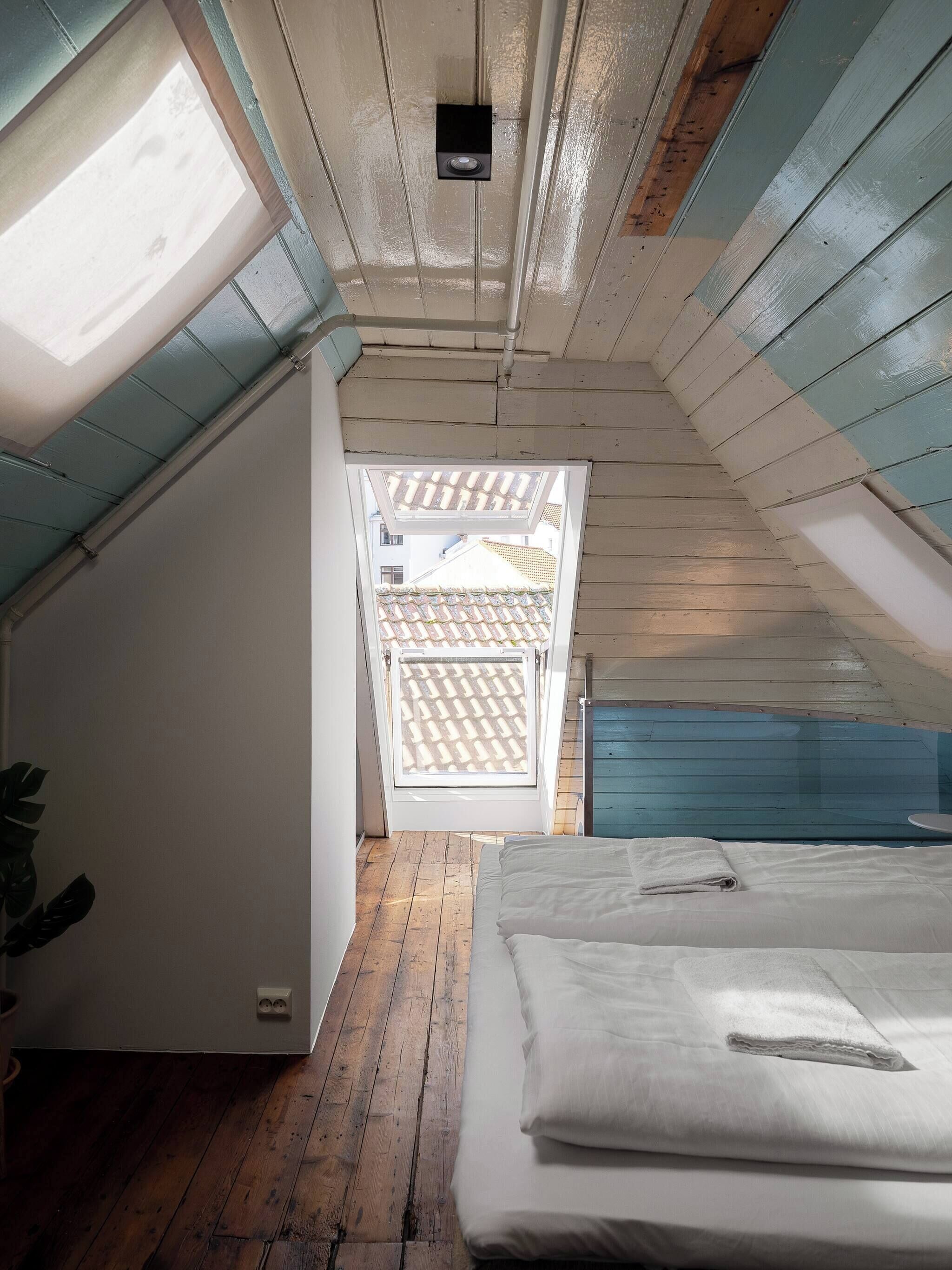 A small attic bedroom with a sloped ceiling, a skylight, a bed, and a view of the outside through a door.