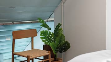 Quarto com teto inclinado, uma cadeira de madeira, um vaso de planta e uma cama.