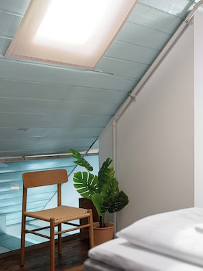 Een kamer met een schuine kap, een houten stoel, een potplant en een bed.