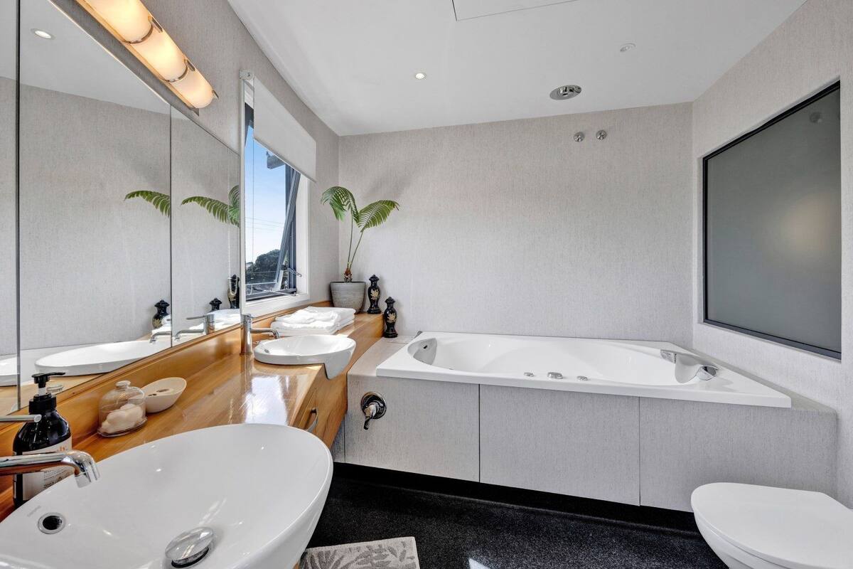 Un baño moderno con un espejo grande, dos lavamanos, una bañera y un inodoro.
