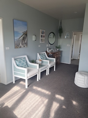 Une pièce comprenant deux fauteuils blancs, une petite table, une commode et un miroir au mur.