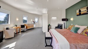 A modern hotel room with a bed, a desk, a chair, a small table, and a view of the outdoors.