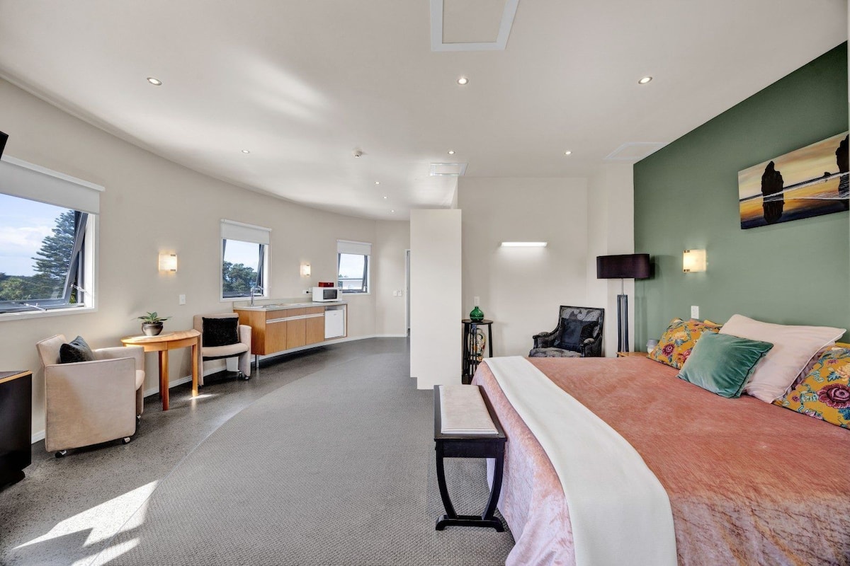 Una habitación de hotel moderna con una cama, un escritorio, una silla, una mesita y vistas al exterior.