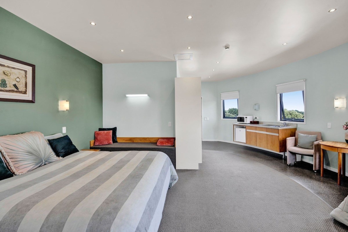 Una habitación de hotel moderna con cama, sofá, kitchenette y vistas al exterior.