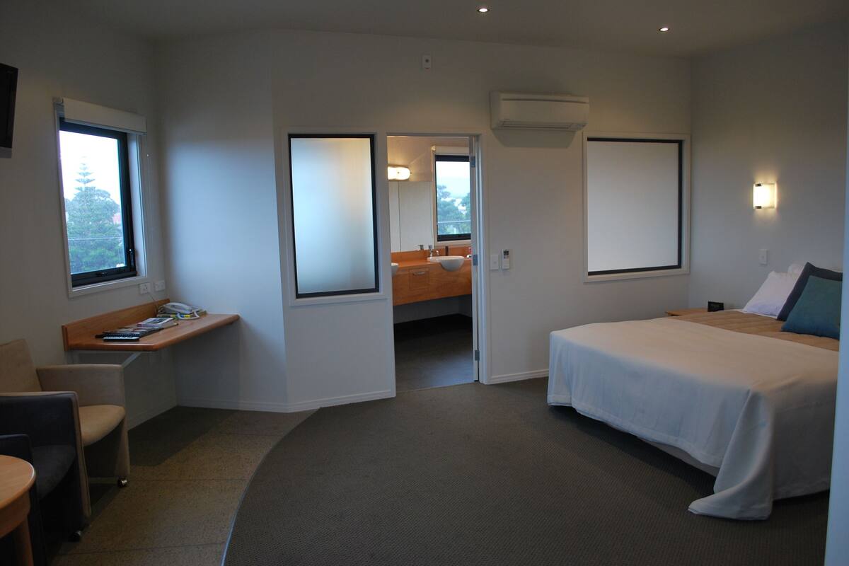 Una habitación de hotel con cama, escritorio, silla y baño visible a través de una puerta abierta.