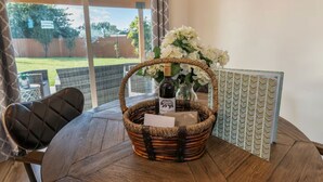 Een rieten mand met een fles en bloemen op een tafel, een stoel en een behang met patroon.