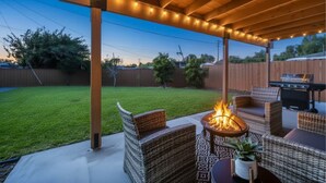 Een terras buiten met rieten meubilair, een vuurkorf en een barbecue.