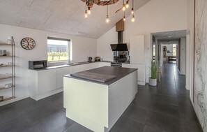 Eine moderne Küche mit einer zentralen Kochinsel, einer Wanduhr und Blick ins Freie.