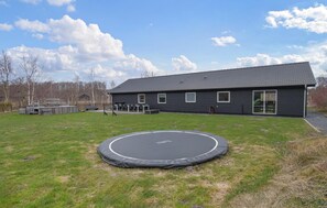 Ein Haus mit Trampolin im Garten, einer überdachten Sitzgelegenheit und einem großen Fenster.