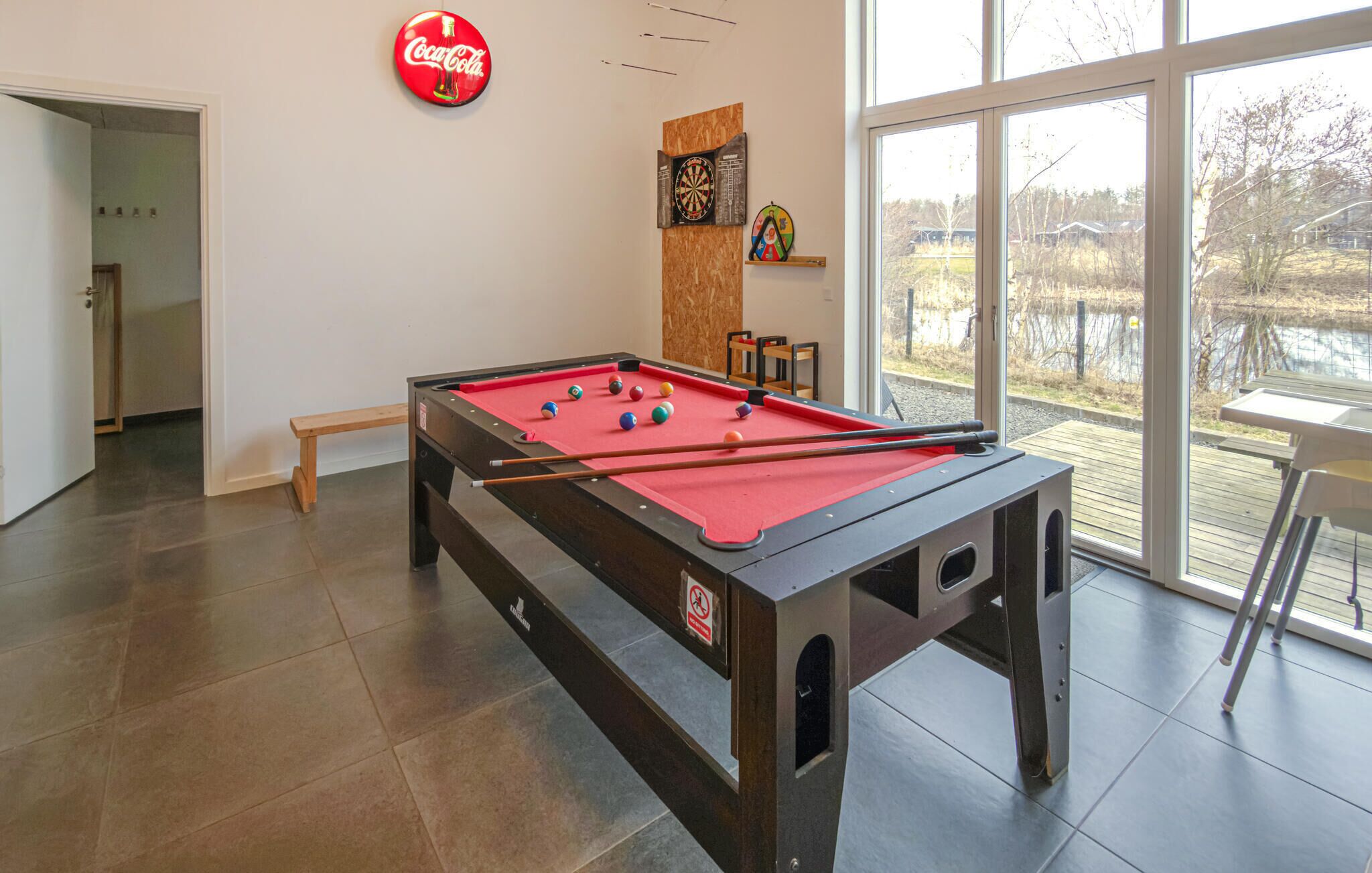 A pool table with a red felt surface, a Coca-Cola sign, and a dartboard on the wall.