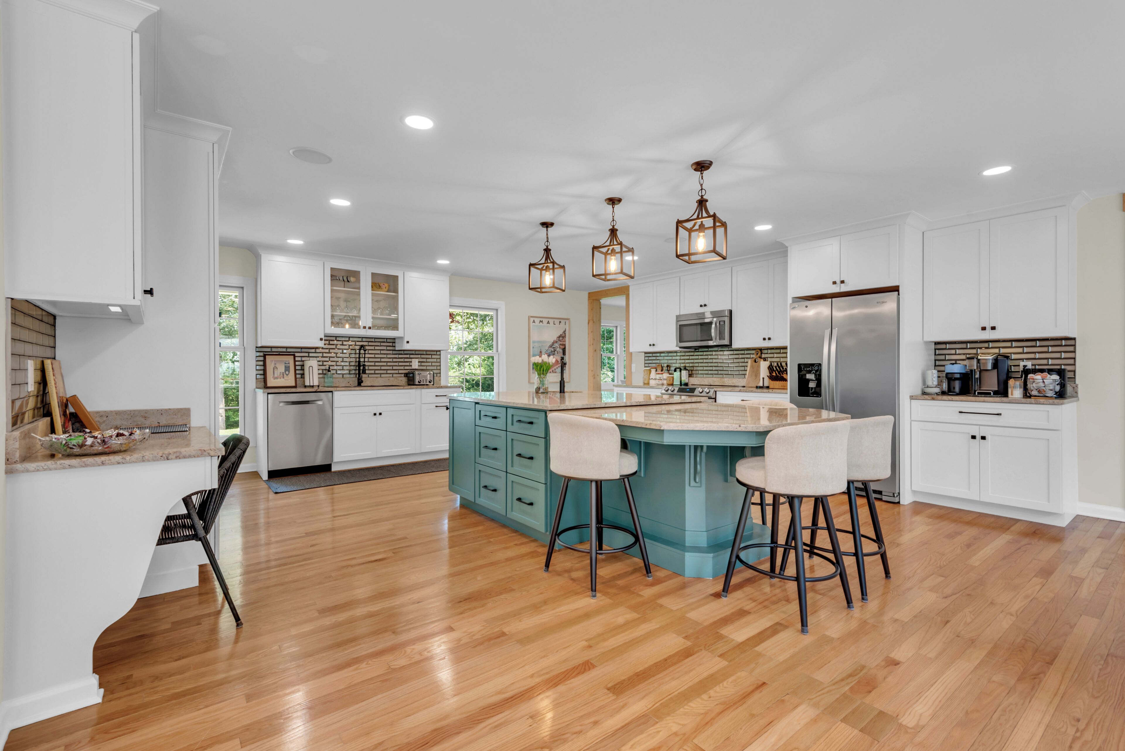 A spacious kitchen with a central island, white cabinetry, and a wooden floor.
