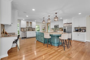 Una cocina amplia con una isla central, armarios blancos y piso de madera.
