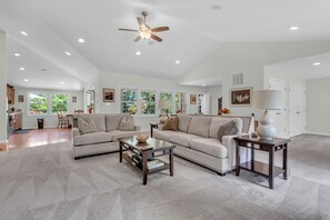 A spacious living room with a high ceiling, large windows, and a ceiling fan. - The Harness Creek House (Annapolis)