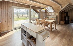 Un interior de madera con comedor, cocina equipada con estufa y un amplio ventanal con vistas a árboles.
