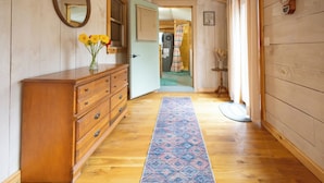 A wooden hallway with a dresser, a mirror, a vase with flowers, and a patterned rug.