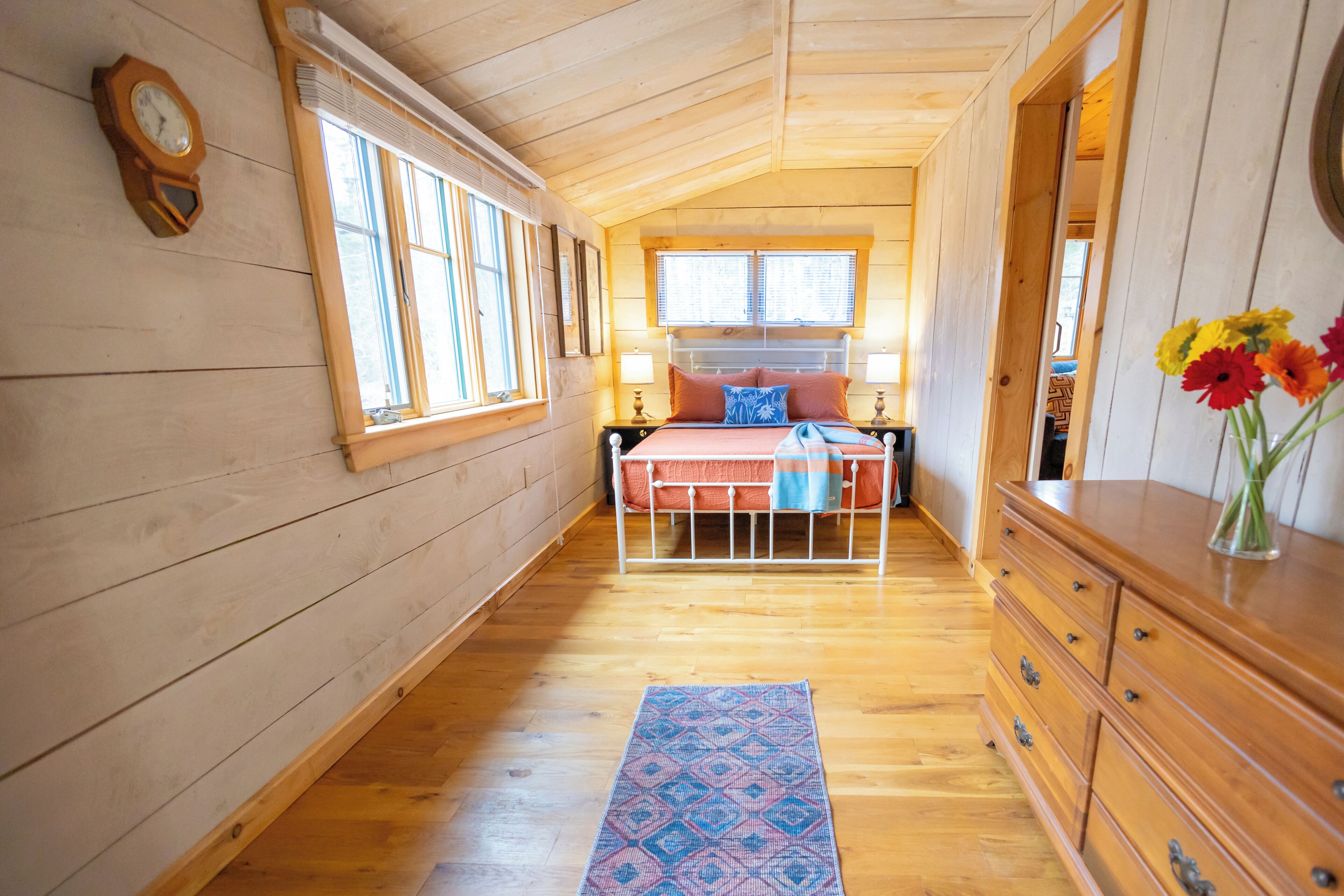 Een slaapkamer in een houten hut met een bed, een kapstok en een klok aan de muur.